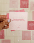 Different tones of pink cards that each have an uplifting affirmation on them for you to read and stick on the walls of your shower.