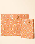 On an ivory background is two orange gift bags with an orange daisy pattern.