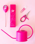 A variety of bright pink gardening tools such as mini plant snips, pruning shear, moisture meter and a metal watering can are shown against a light pink background.