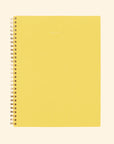 A yellow spiral bound notebook with small gold foiled text in the center that reads, "notebook" as well as grid lined single sided pages.