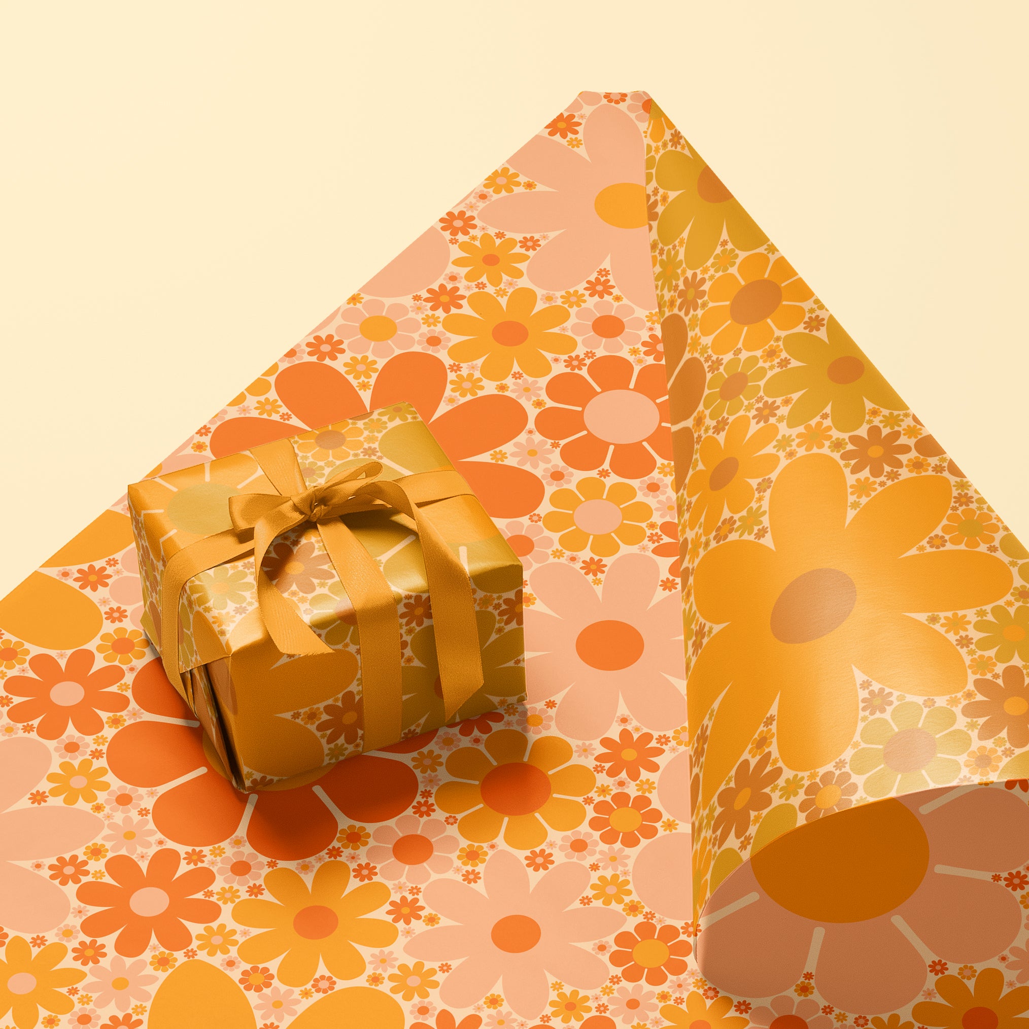 Sheet of wrapping paper filled with orange and yellow flower print. The sheet is bent forward, revealing the other side of the wrapping paper. The back side is covered in the same floral print in pink and oranges.