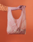 A light pink nylon reusable tote bag with an alocasia leaf print.