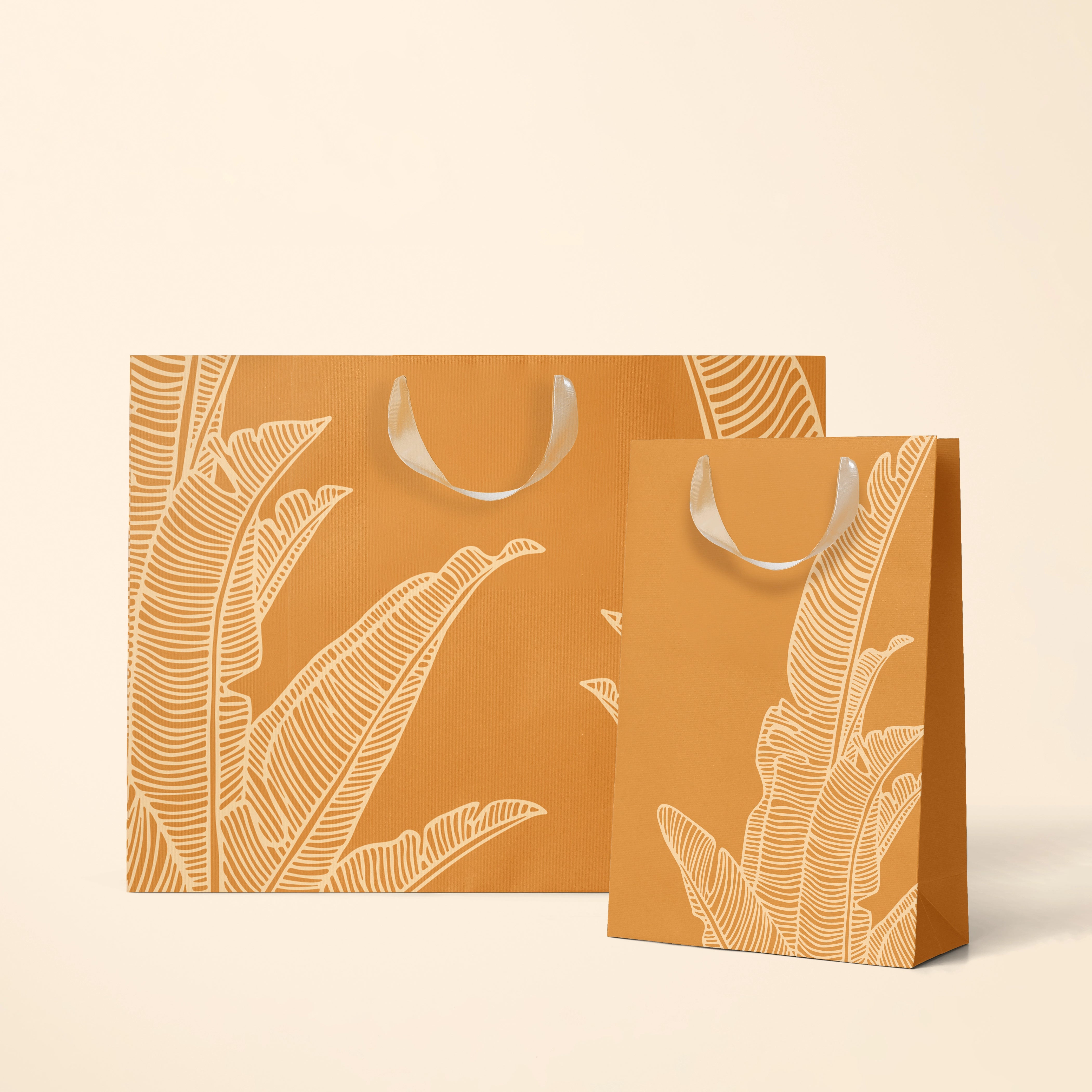 On a cream background is two different sized orange gift bags with a cream bird of paradise line drawing design as well as cream ribbon handles. 