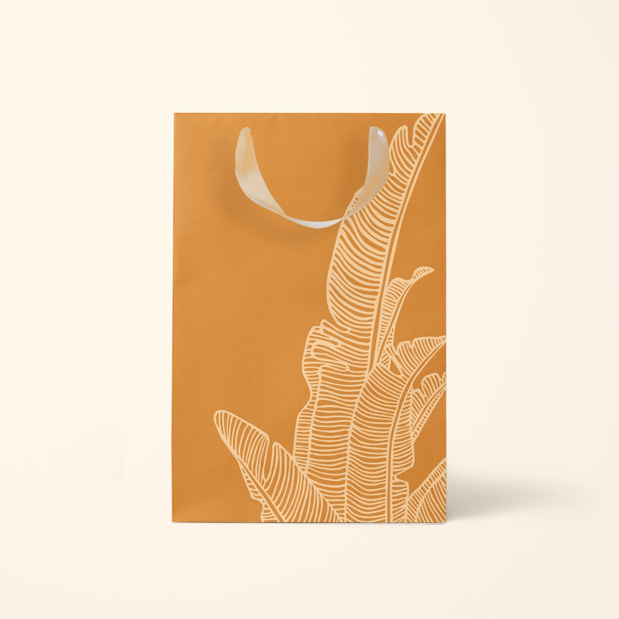 The medium orange gift bag with a cream bird of paradise line drawing design as well as cream ribbon handles.