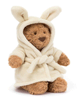 On a white background is a brown stuffed animal bear wearing a fuzzy white rope with bunny ears.