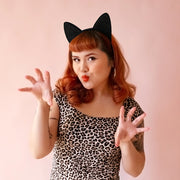 Model in leopard body suit with red hair wears a black glitter cat ears headband.