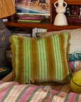 A green striped pillow with fringe detailing around the edges.