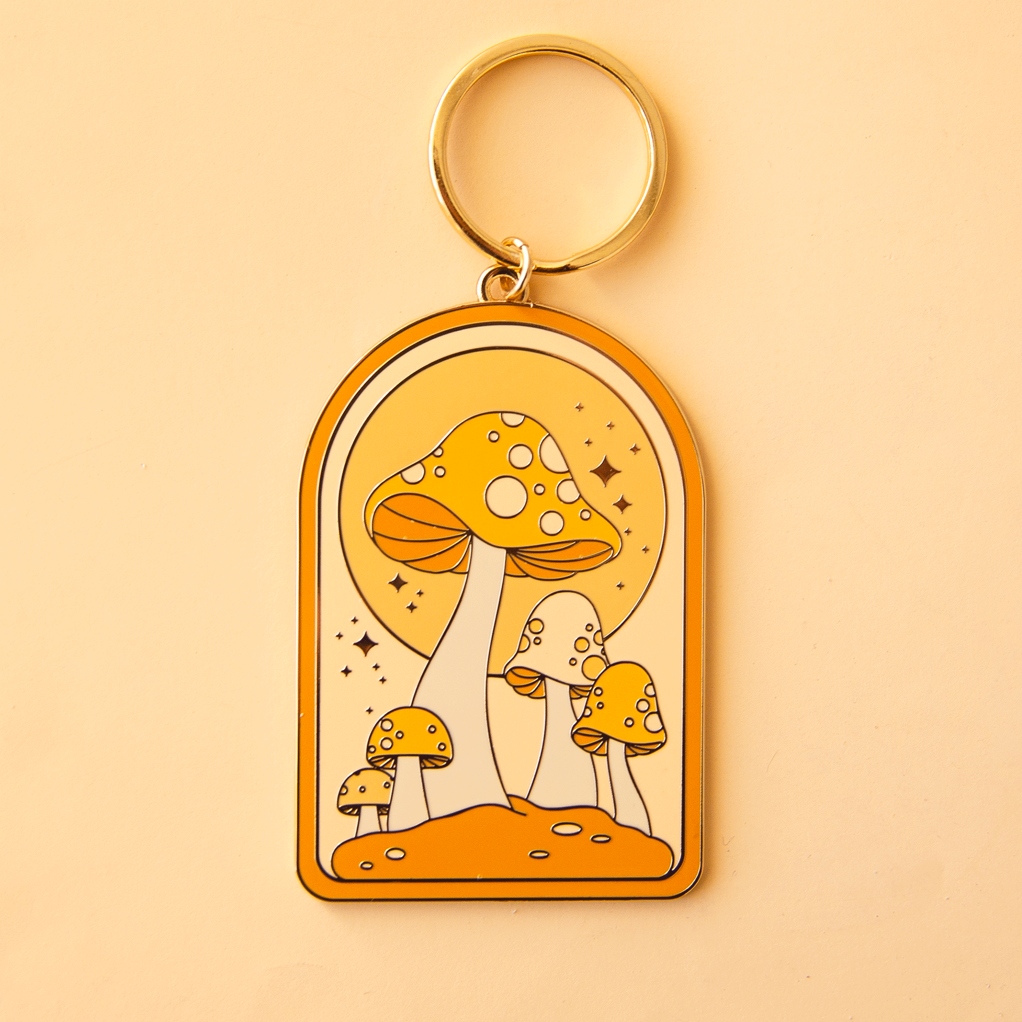 On a yellow background is an arched metal keychain is a gold loop and a mushroom design. 