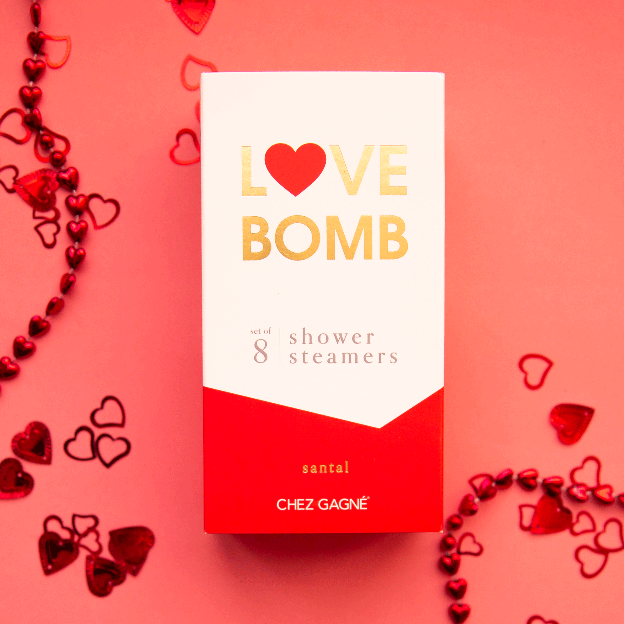 On a red background is a white and red box of shower steaming tablets with text at the top that reads, &quot;Love Bomb 8 Shower Steamers&quot;.