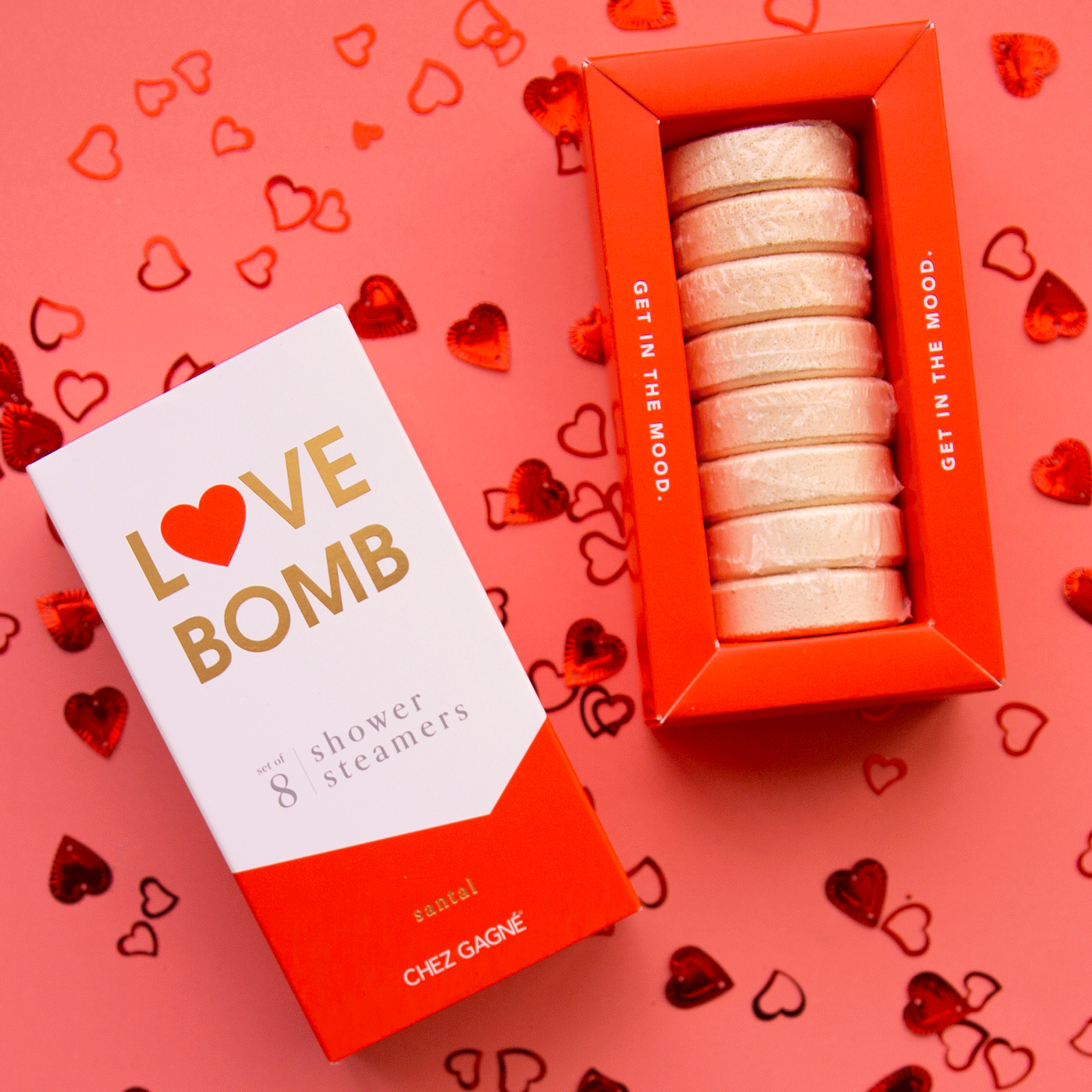On a red background is a white and red box of shower steaming tablets with text at the top that reads, "Love Bomb 8 Shower Steamers".