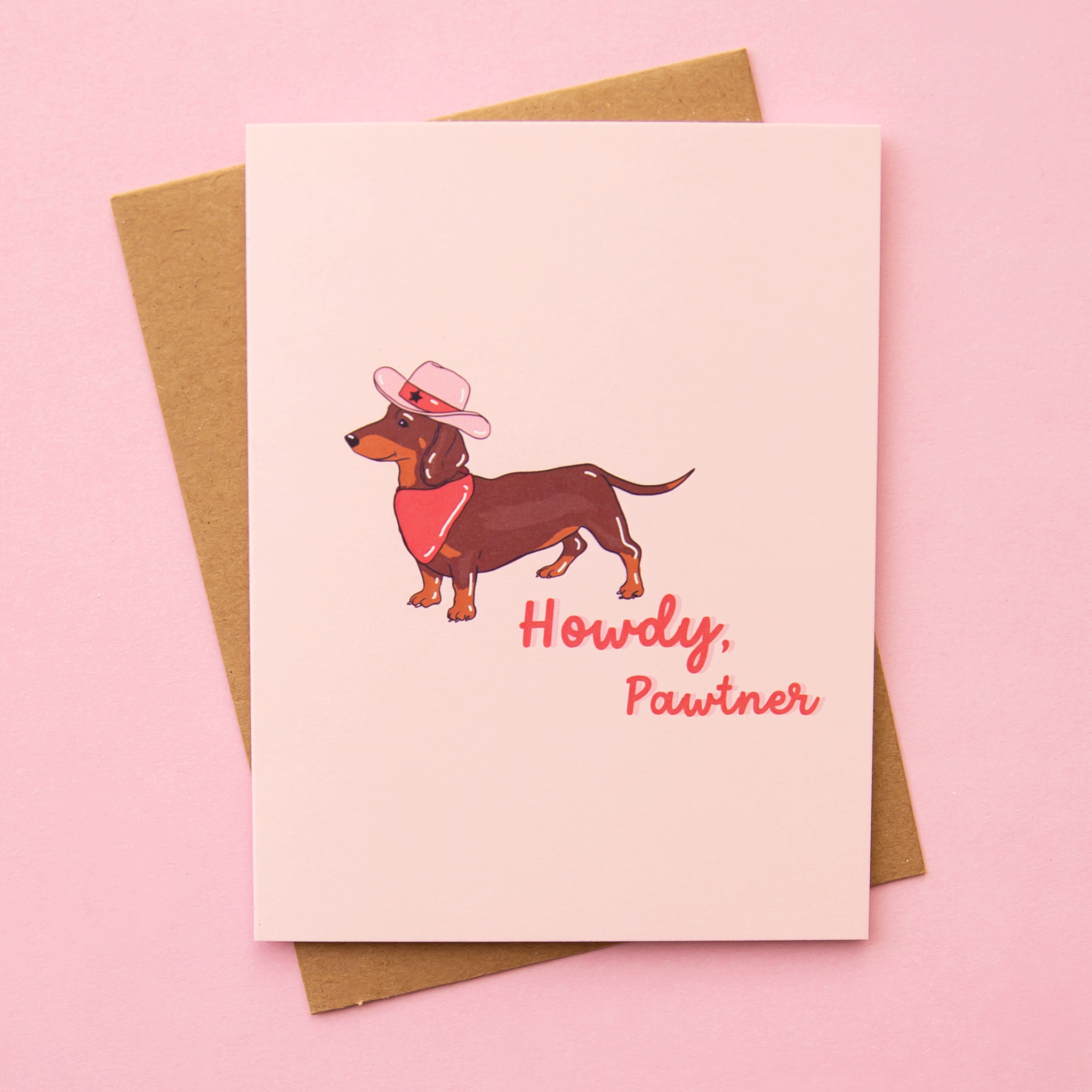 On a pink background is a light pink card with an image of a Weiner dog in a pink bandana and a western cowgirl hat along with pink cursive text to its right that reads, "Howdy Partner".