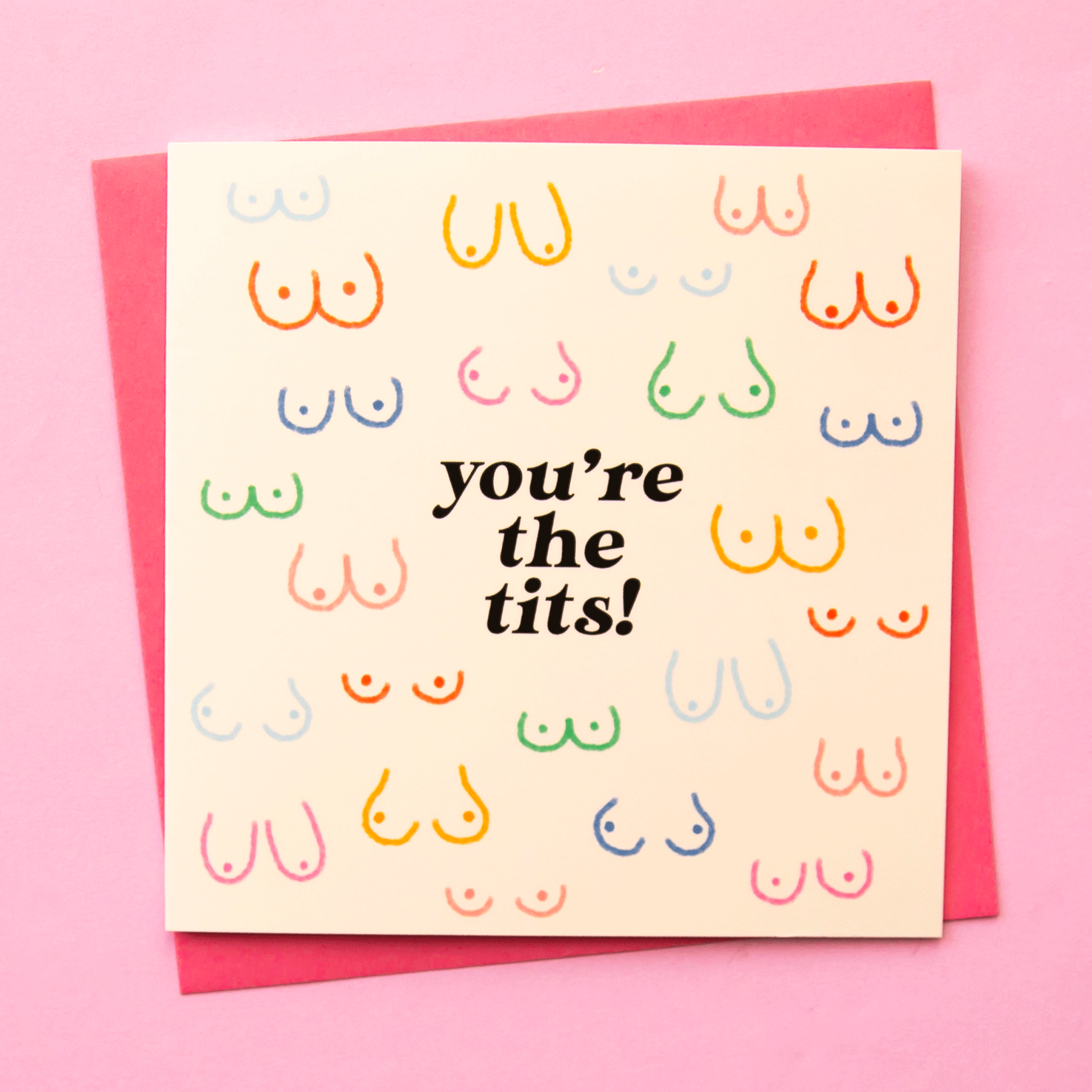 The text reads, &quot;You&#39;re the tits!&quot; on a white card with different colored breast illustrations that vary in all different sizes and shapes. The colors include light blue, dark blue, green, mustard, red and pink! A pink envelope is also shown and included with purchase.