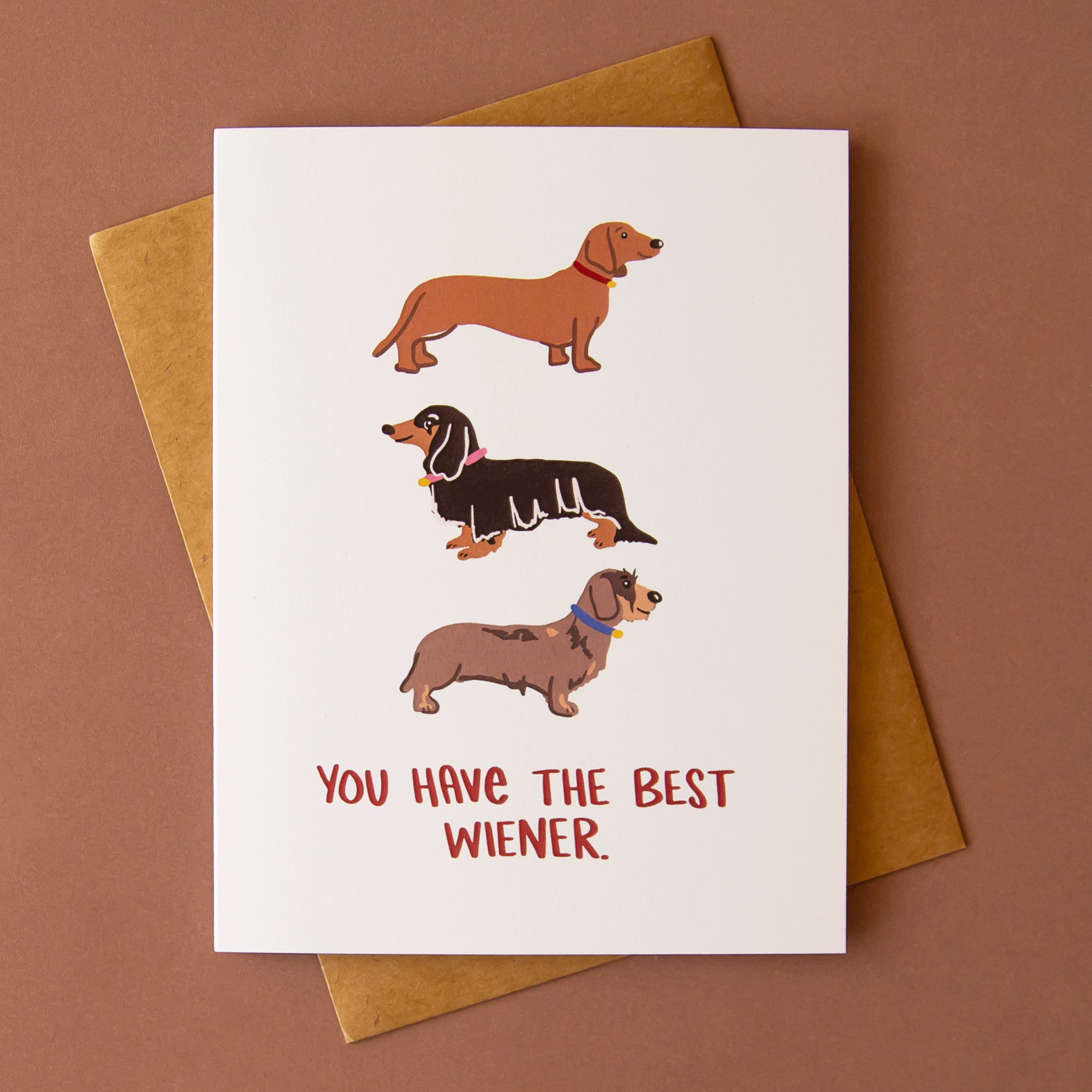 On a brown background is a white card with three different wiener dog illustrations with text on the bottom that reads, &quot;You Have The Best Wiener.&quot;.
