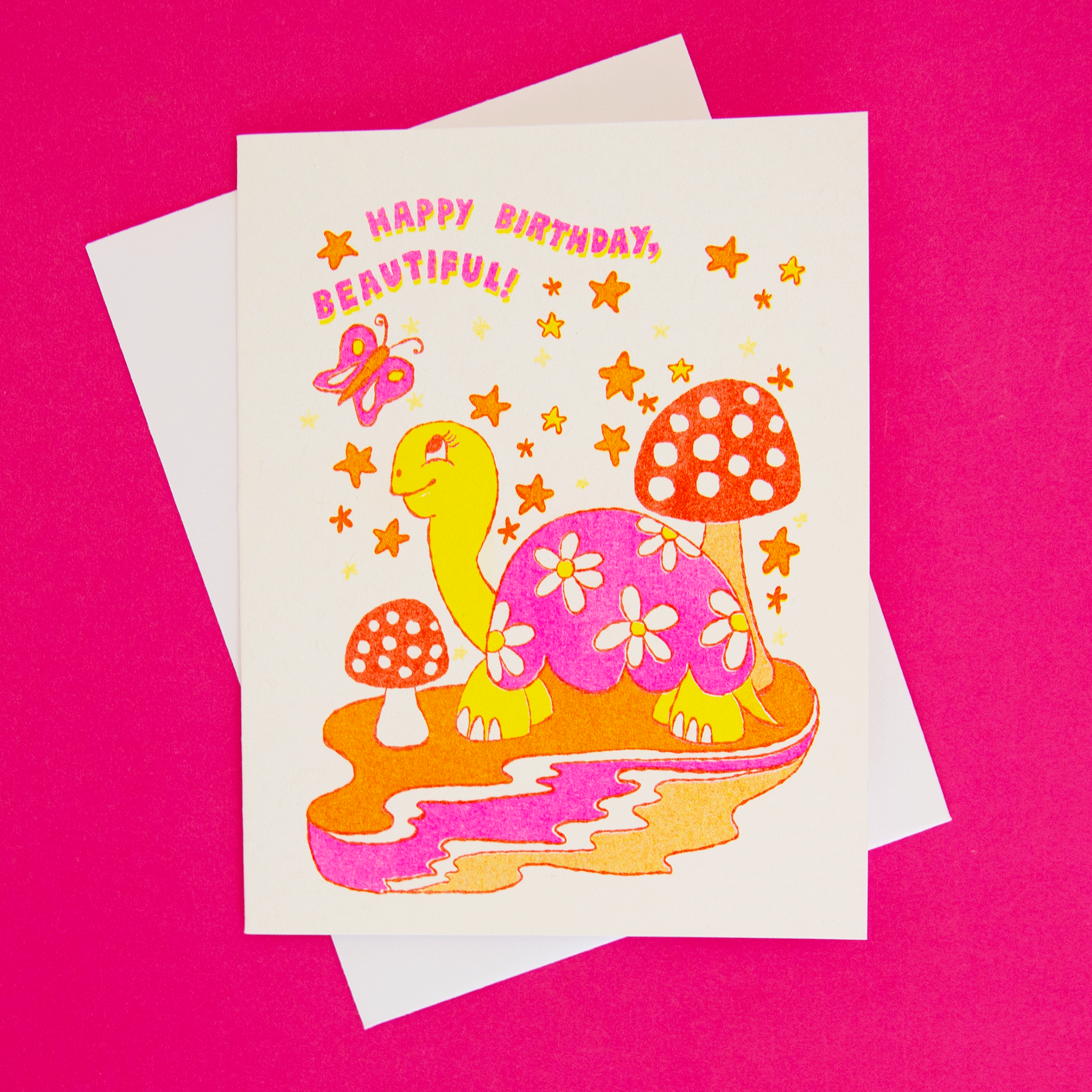  On a coral background is a white card with a colorful, red, pink and orange turtle illustration surrounded by mushroom, stars and a butterfly along with text that reads, "Happy Birthday Beautiful!".