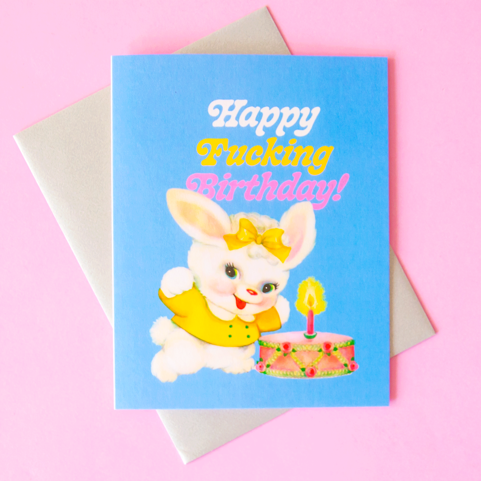 On a pink background is a blue card with text that reads, "Happy Fucking Birthday!" along with a graphic of a white fluffy bunny with a yellow shirt and bow standing next to a vintage birthday cake. 