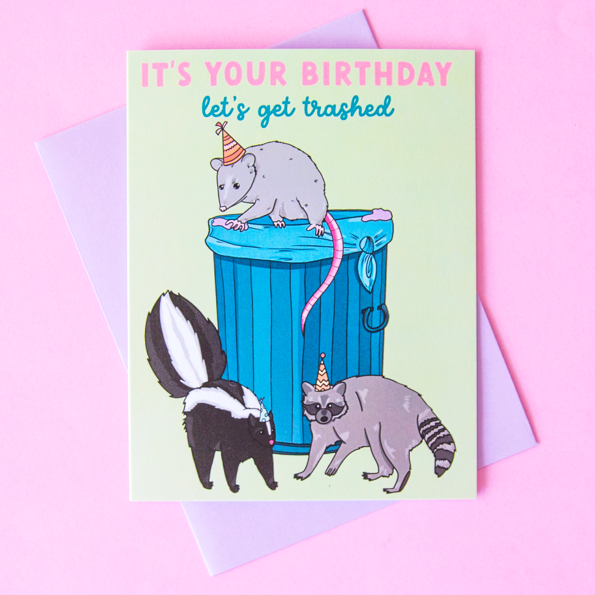 This card reads, "It's Your Birthday Let's Get Trashed" accompanied by an illustration of a possum, skunk and raccoon wearing birthday hats surrounding a trash can.