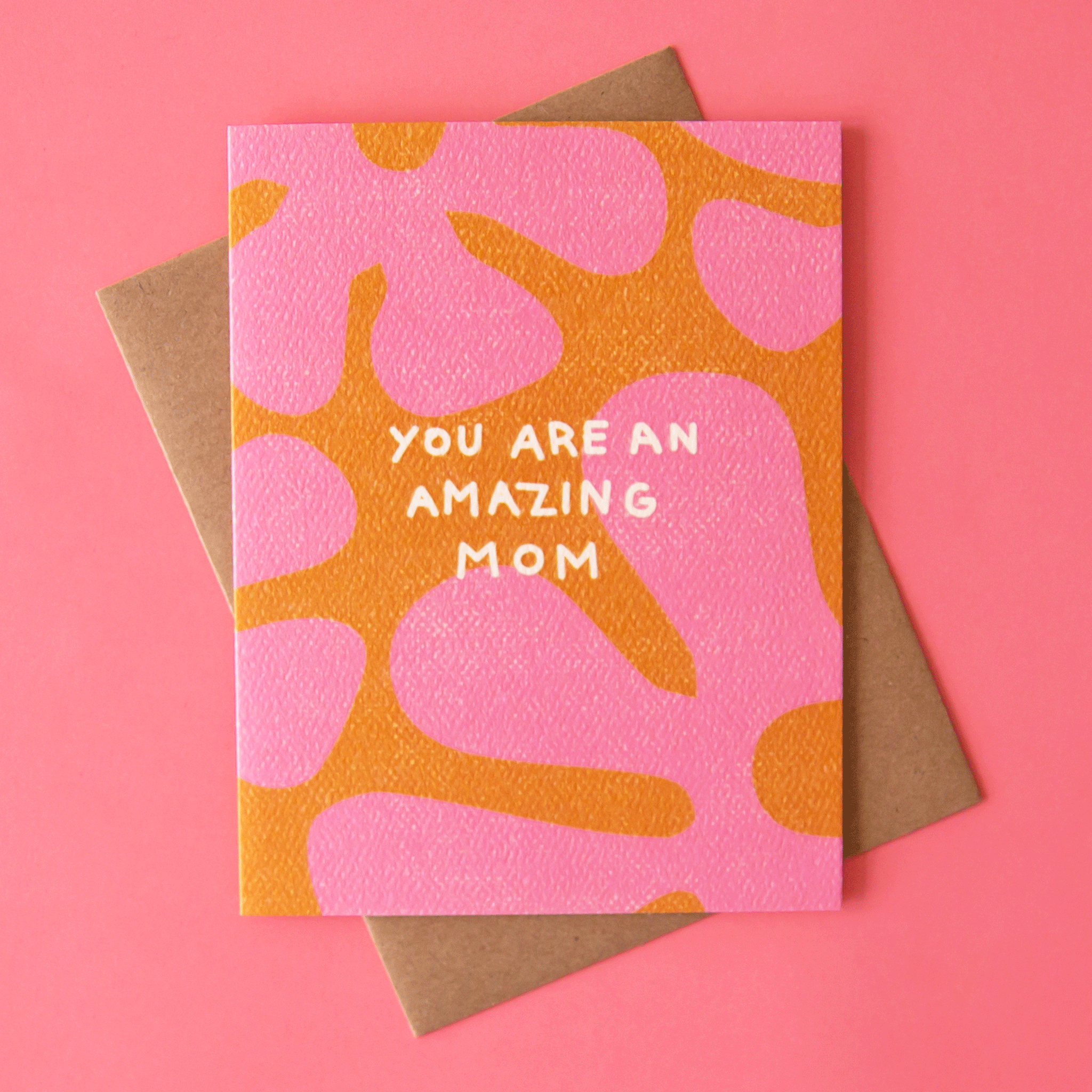  An orange card with a large pink floral print all over the front along with white text in the center that reads, &quot;You Are An Amazing Mom&quot; and a coordinating kraft brown envelope.