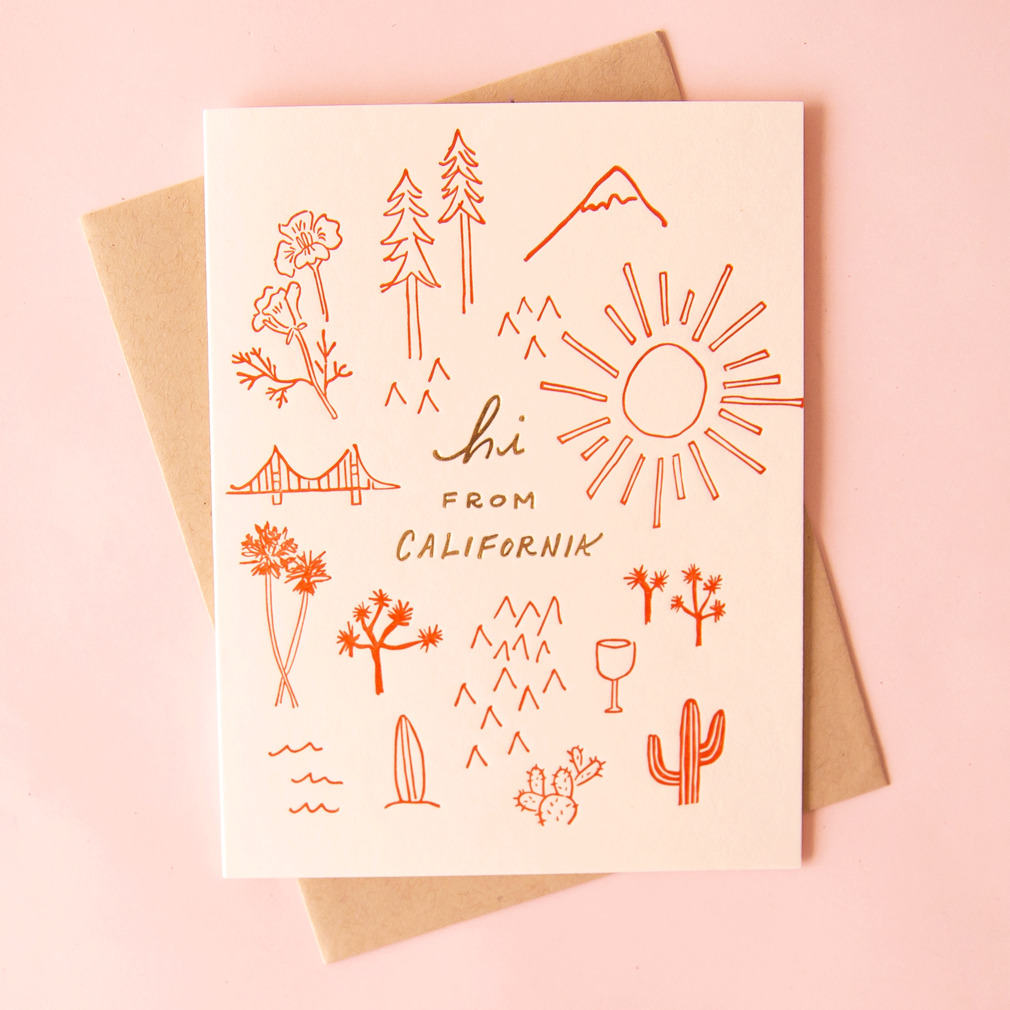 Photo of a cream colored greeting card that reads "hi from California" in gold leaf. Rust colored simple line drawings of poppy flowers, trees, mountains, a sun, cacti, waves and the Golden Gate Bridge surround the writing. The card is laying on a pink surface with 3 match books surrounding the card.