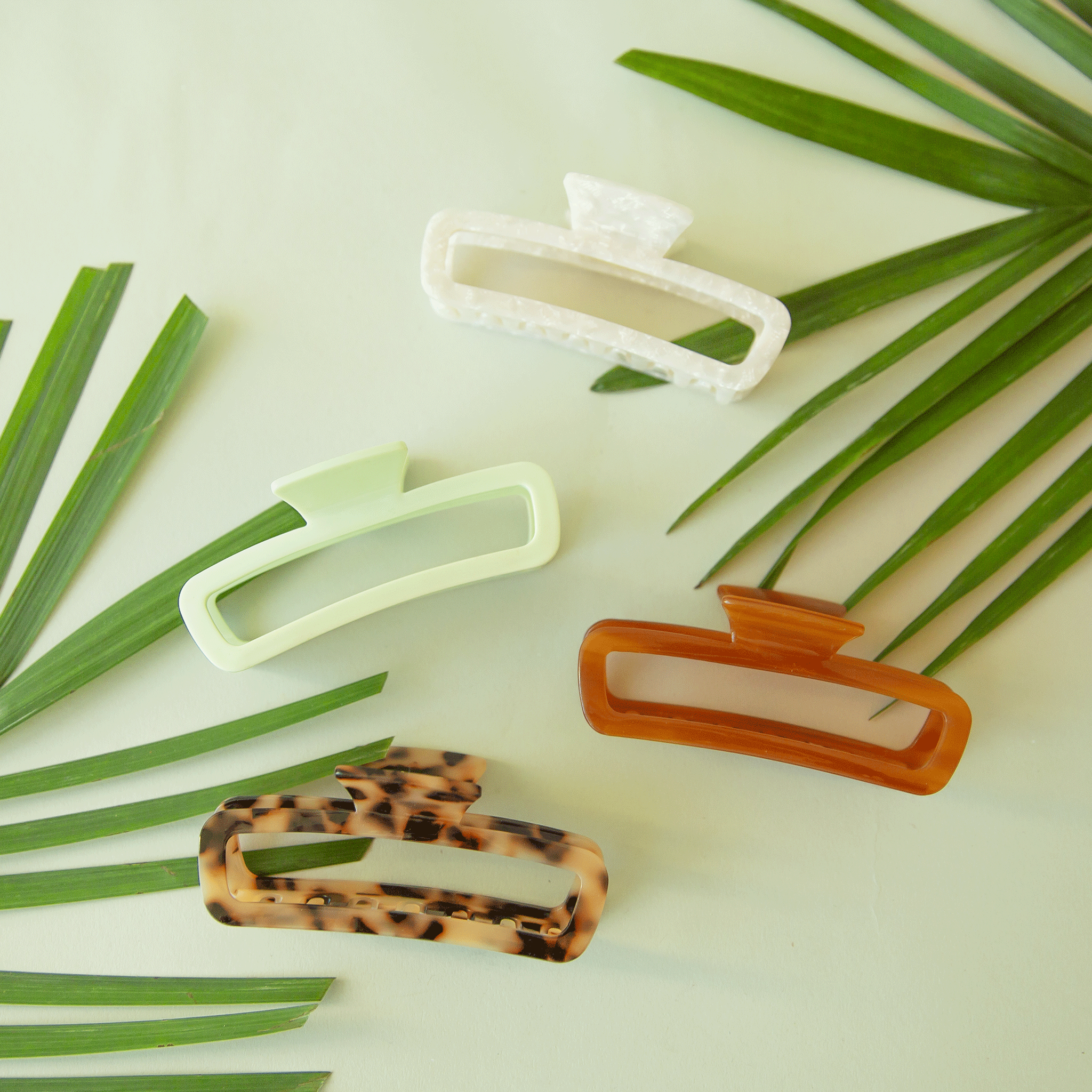On a mint background is the mist cabana hair claw sitting next to three different color ways of the clip.