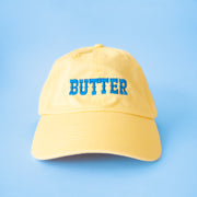A yellow baseball hat with blue text that reads, 'Butter'.