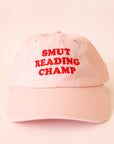 A pink baseball hat with red text that reads, 'Smut Reading Champ'.