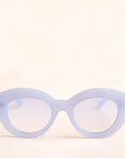 On a neutral background is the Gemma Sunglasses in a light blue shade. They have a rounded shape with a slight cateye flair at the corners. The frame material is a durable plastic and the lenses are a similar tone.