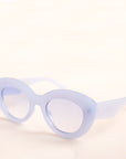 On a neutral background is the Gemma Sunglasses in a light blue shade. They have a rounded shape with a slight cateye flair at the corners. The frame material is a durable plastic and the lenses are a similar tone.