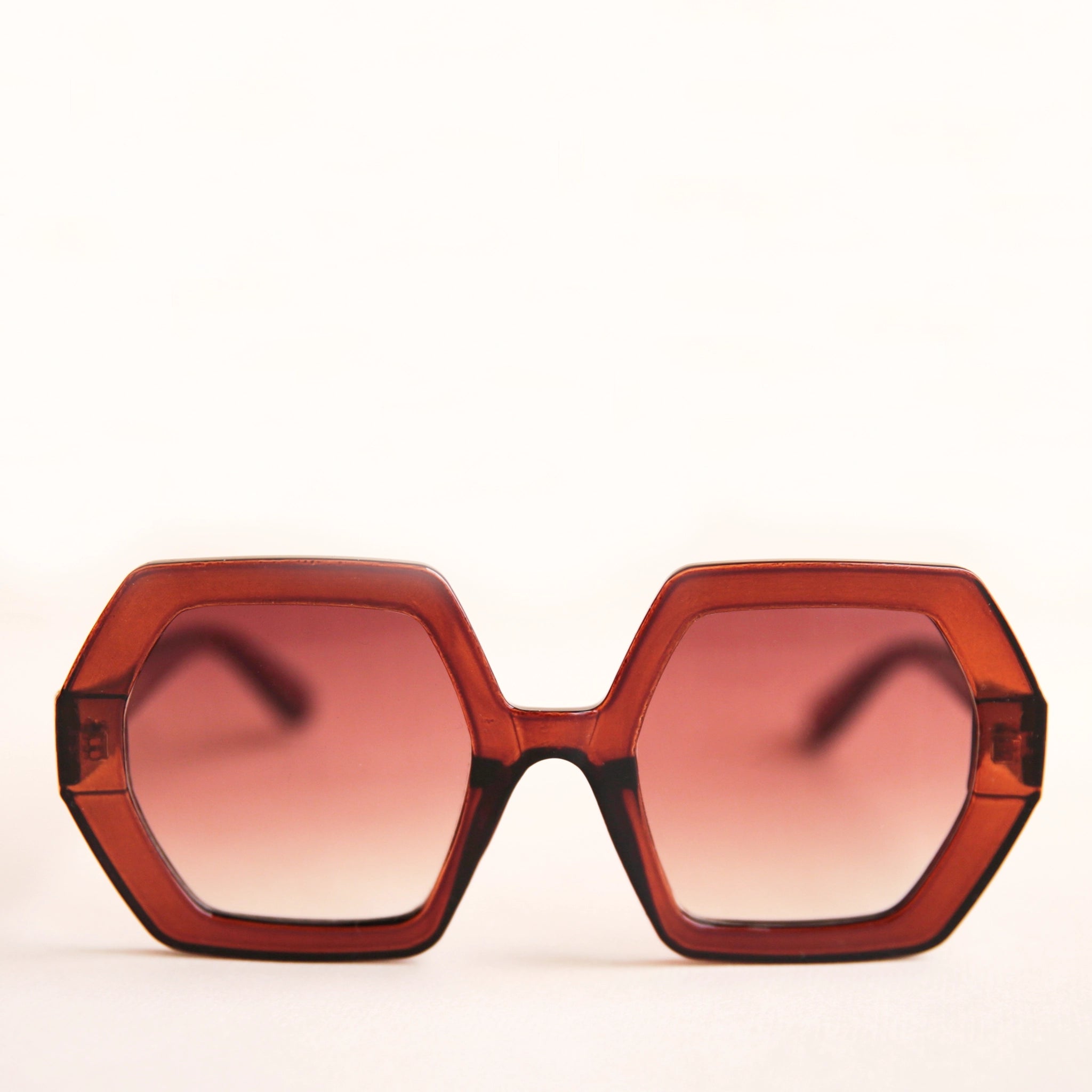On a neutral background is a pair of hexagon shaped sunglasses in a cognac brown color.