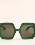 On a neutral background is a pair of hexagon shaped sunglasses in an emerald green color.