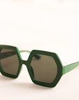 On a neutral background is a pair of hexagon shaped sunglasses in an emerald green color.