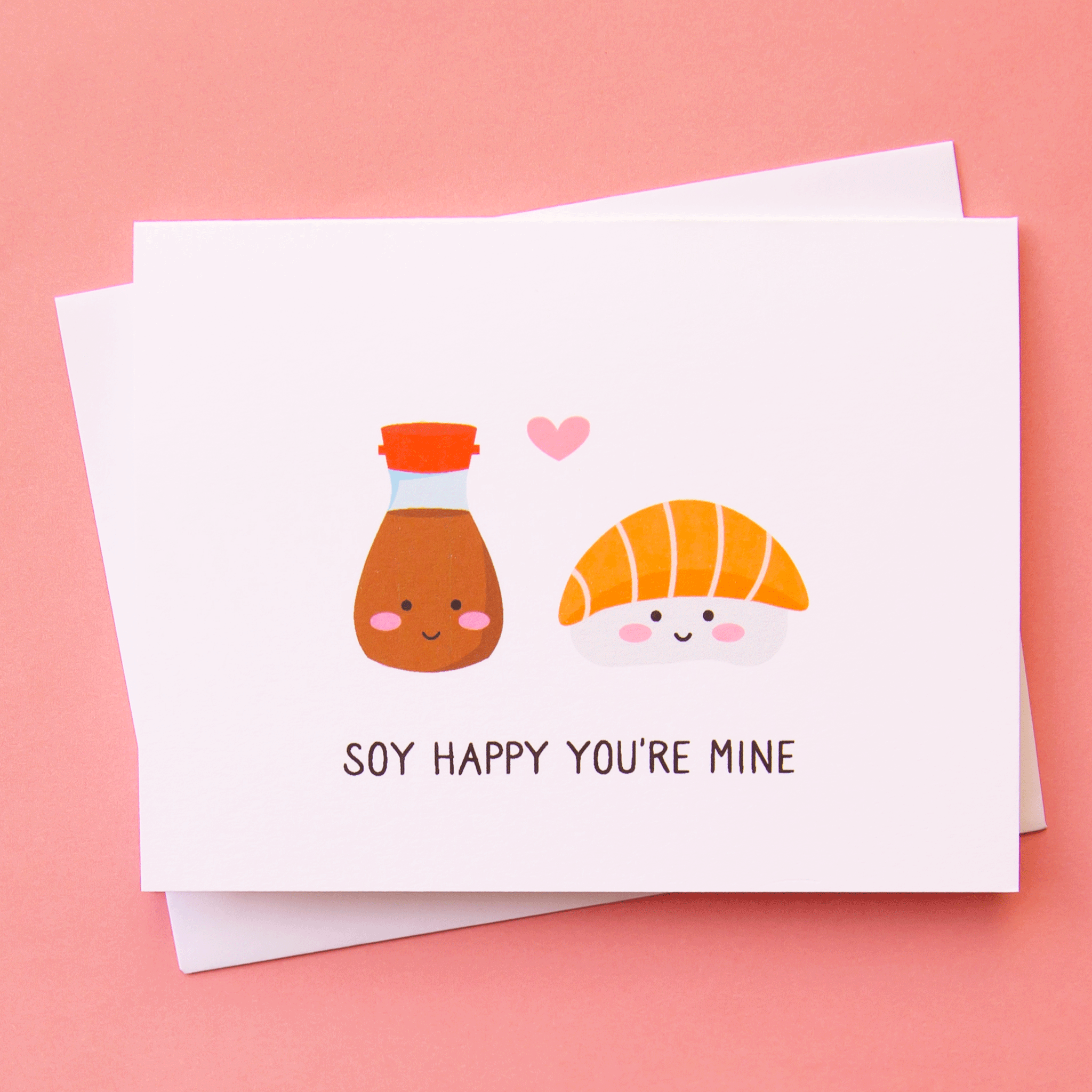 A white card with an illustration of a salmon sashimi and soy sauce both with smiling faces and a small pink heart in between them as well as text underneath that reads, &quot;Soy Happy You&#39;re Mine&quot; in black letters.
