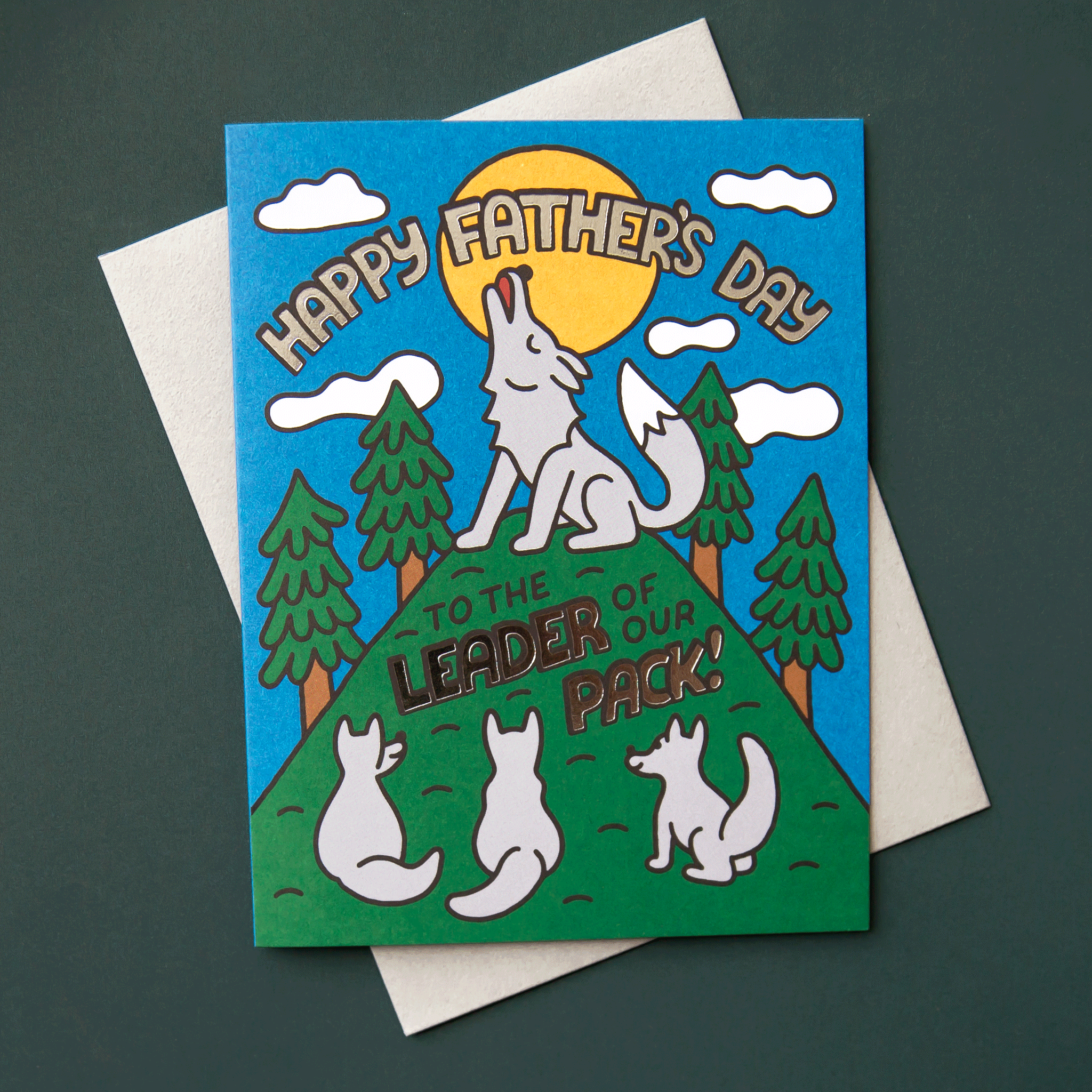 On a dark green background is a blue and green card featuring a graphic of a wolf on top of a hill howling while the pup wolfs are looking up from the bottom and text that reads, "Happy Father's Day To The Leader Of Our Pack!".