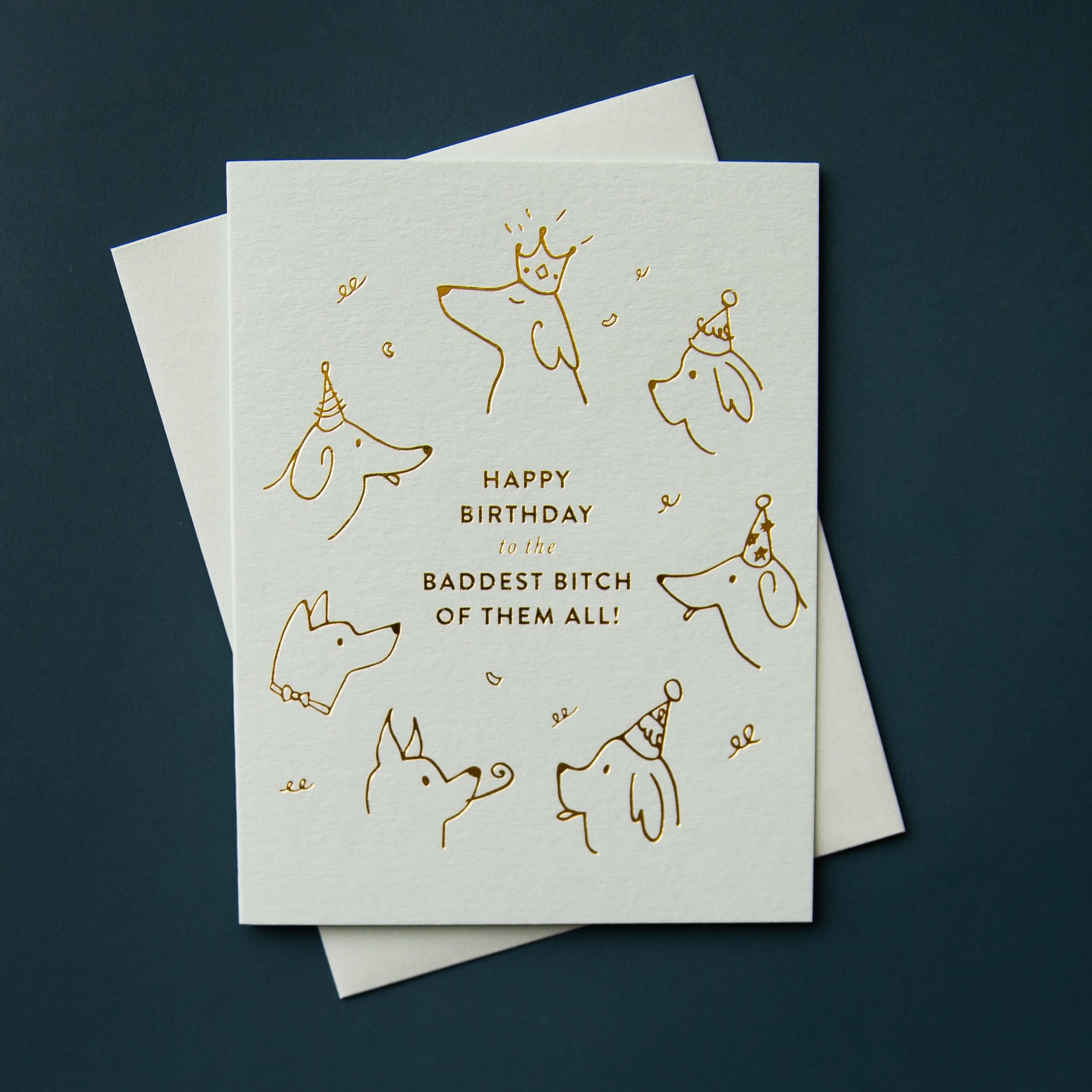 Light blue illustrated greeting card with matching envelope. The illustration is of sketchy dog heads wearing party hats, in gold foil, with text "Happy Birthday to the Baddest Bitch of Them All!"