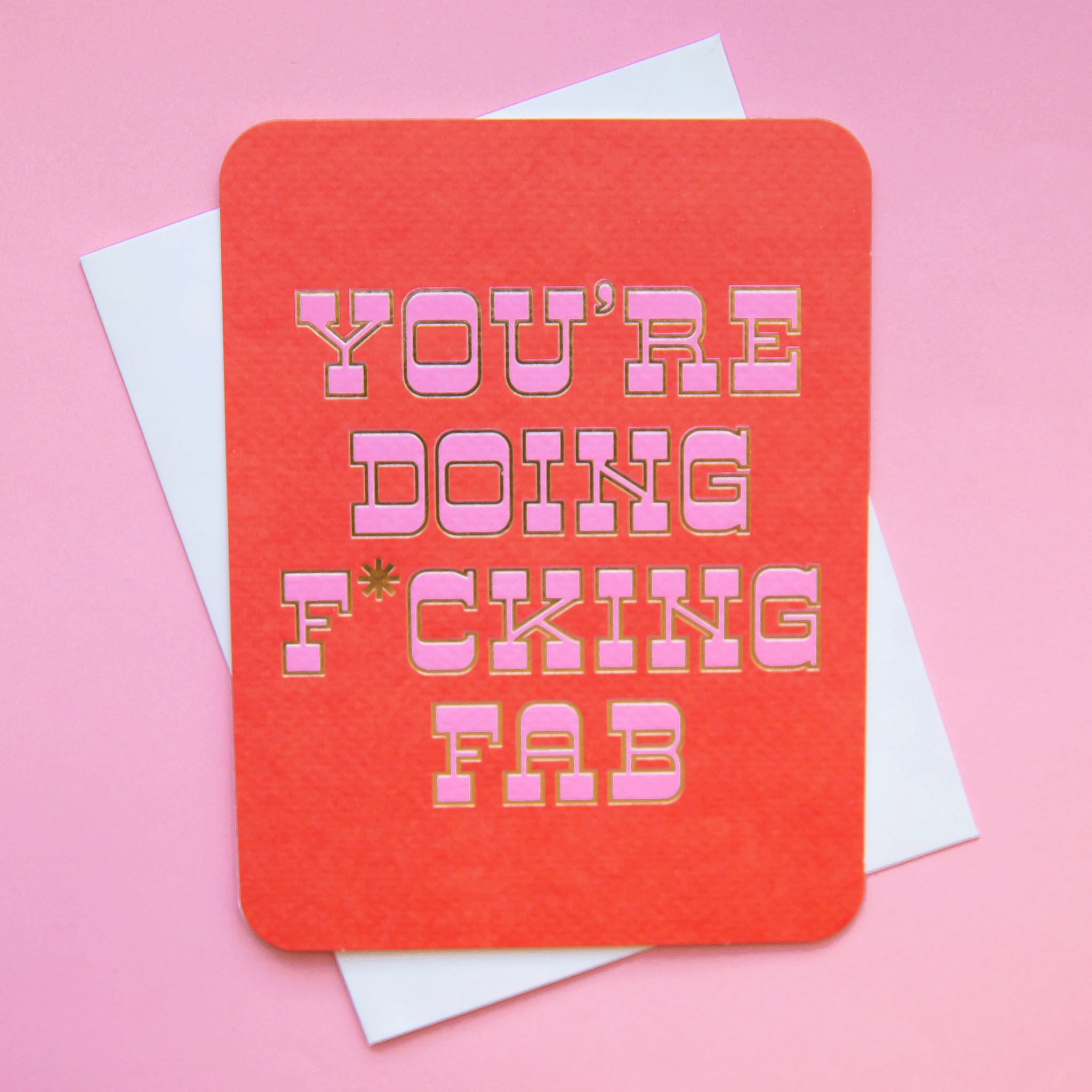 A red card with pink western style text that reads, "You're Doing F*cking Fab" along with a white envelope.
