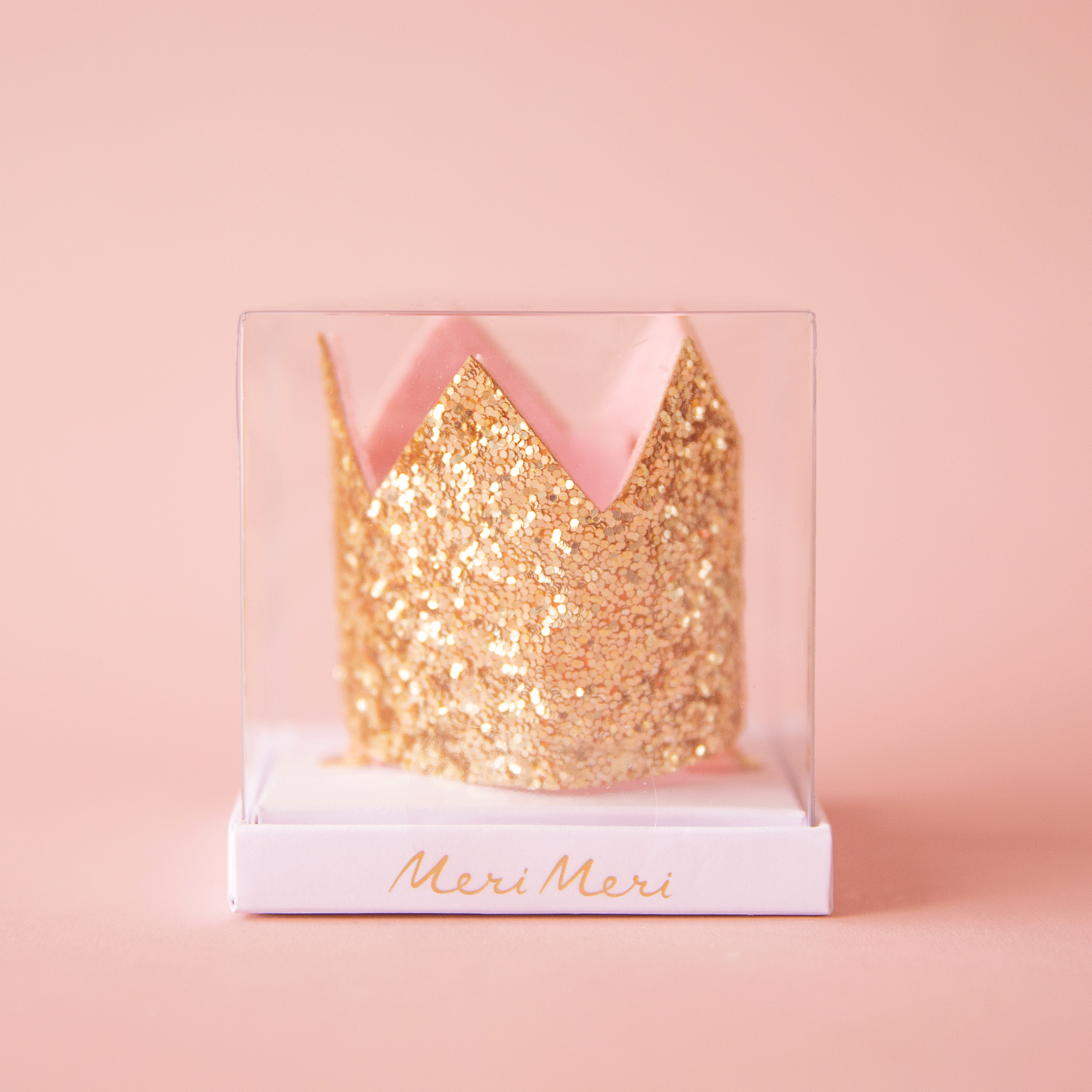 On a pink background is a gold crown shaped hair clip.