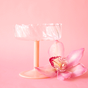 On a pink background is a wavy glass coupe with a pink stem.
