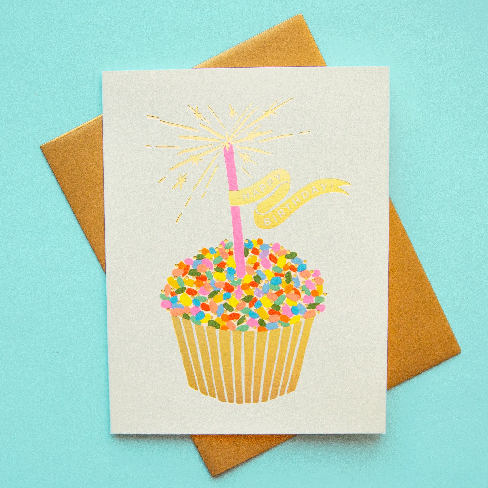 A cupcake birthday card with brown envelope - rainbow cupcake, with sparkling candle print, happy birthday text.