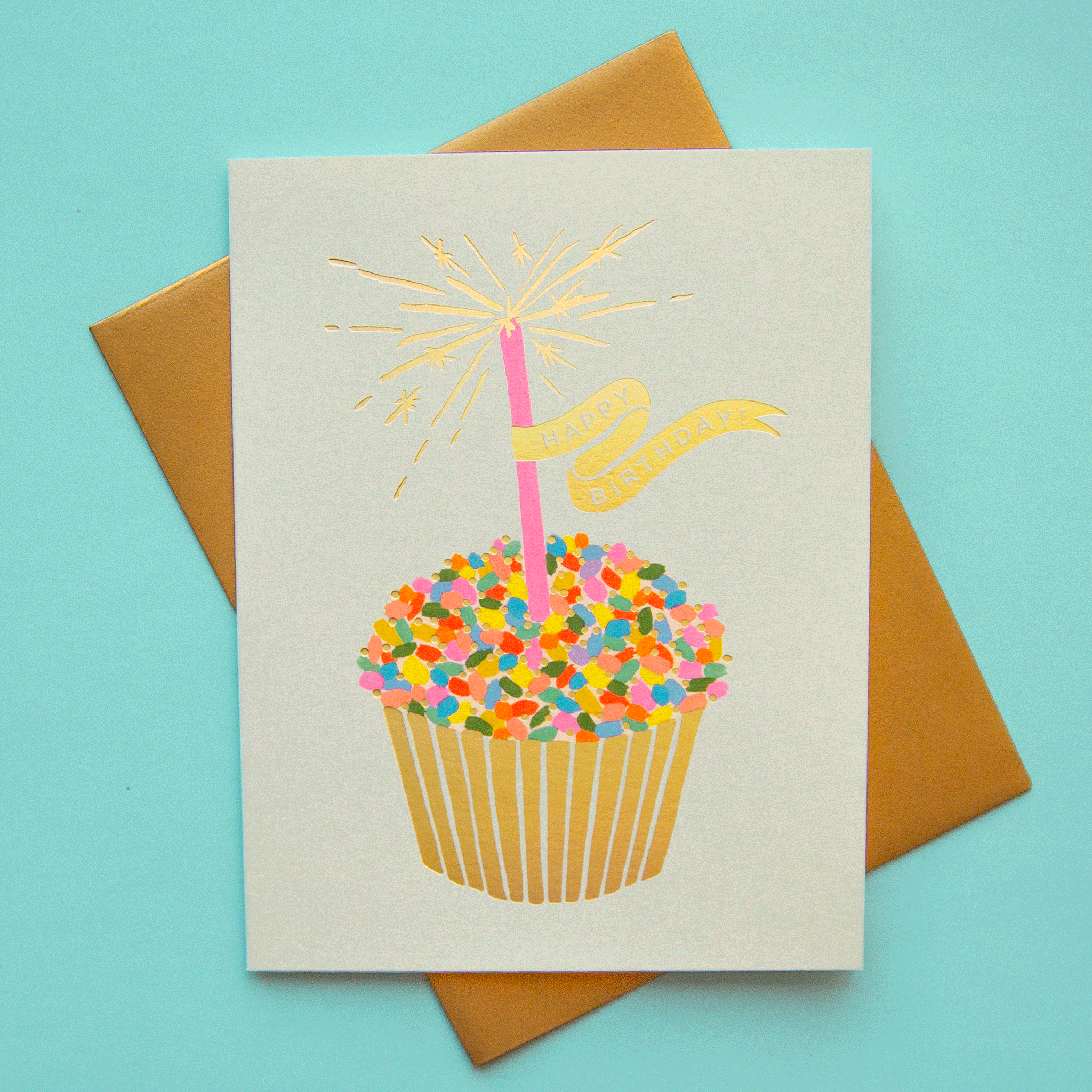A cupcake birthday card with brown envelope - rainbow cupcake, with sparkling candle print, happy birthday text.
