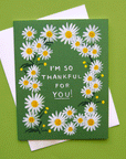 A photograph of a green card and a white envelope behind it. The card has a white daisy border around white text in the center that reads, "I'm So Thankful For You!".