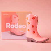 On a peach background is a pink ceramic cowboy boot shaped incense holder with a red flower print.