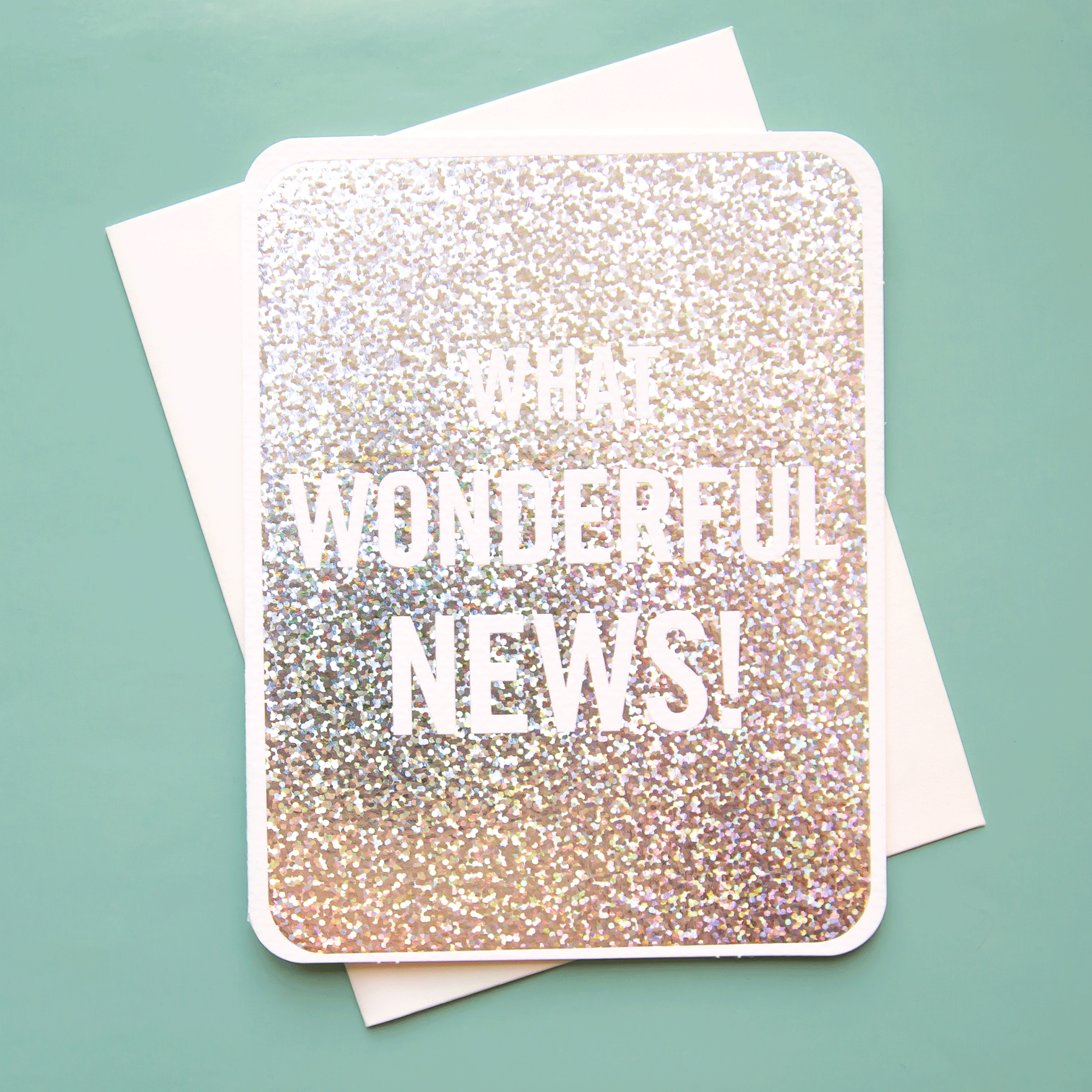 On a green background is a silver card with white text that reads, &quot;What Wonderful News!&quot;. 
