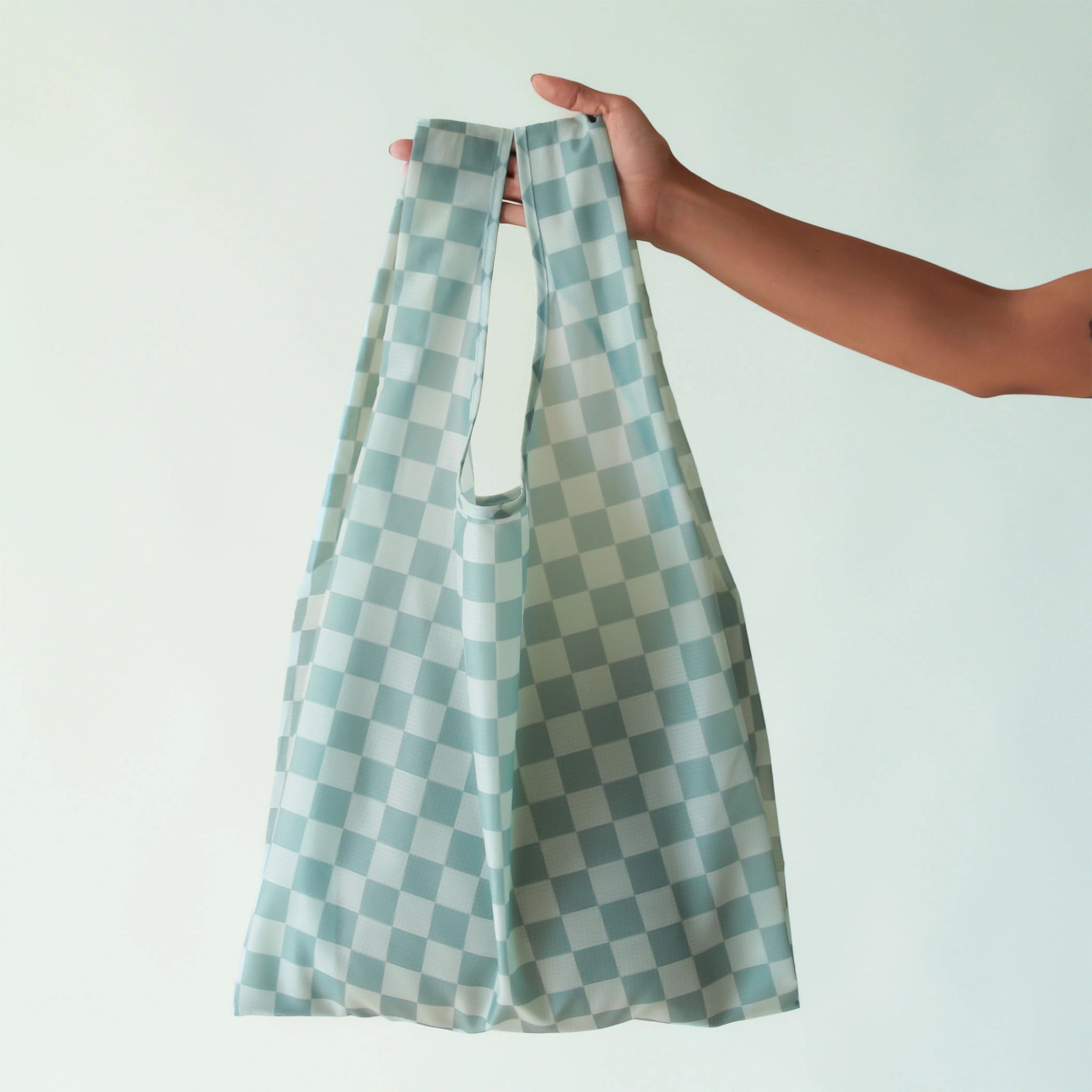 On a light blue background is a turquoise and light blue checkered print nylon bag.