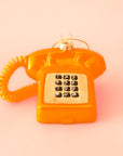 A touch tone phone ornament in a shiny orange color on a bright orange background.