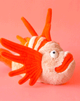 On a coral background is orange lionfish shaped stuffed toy.