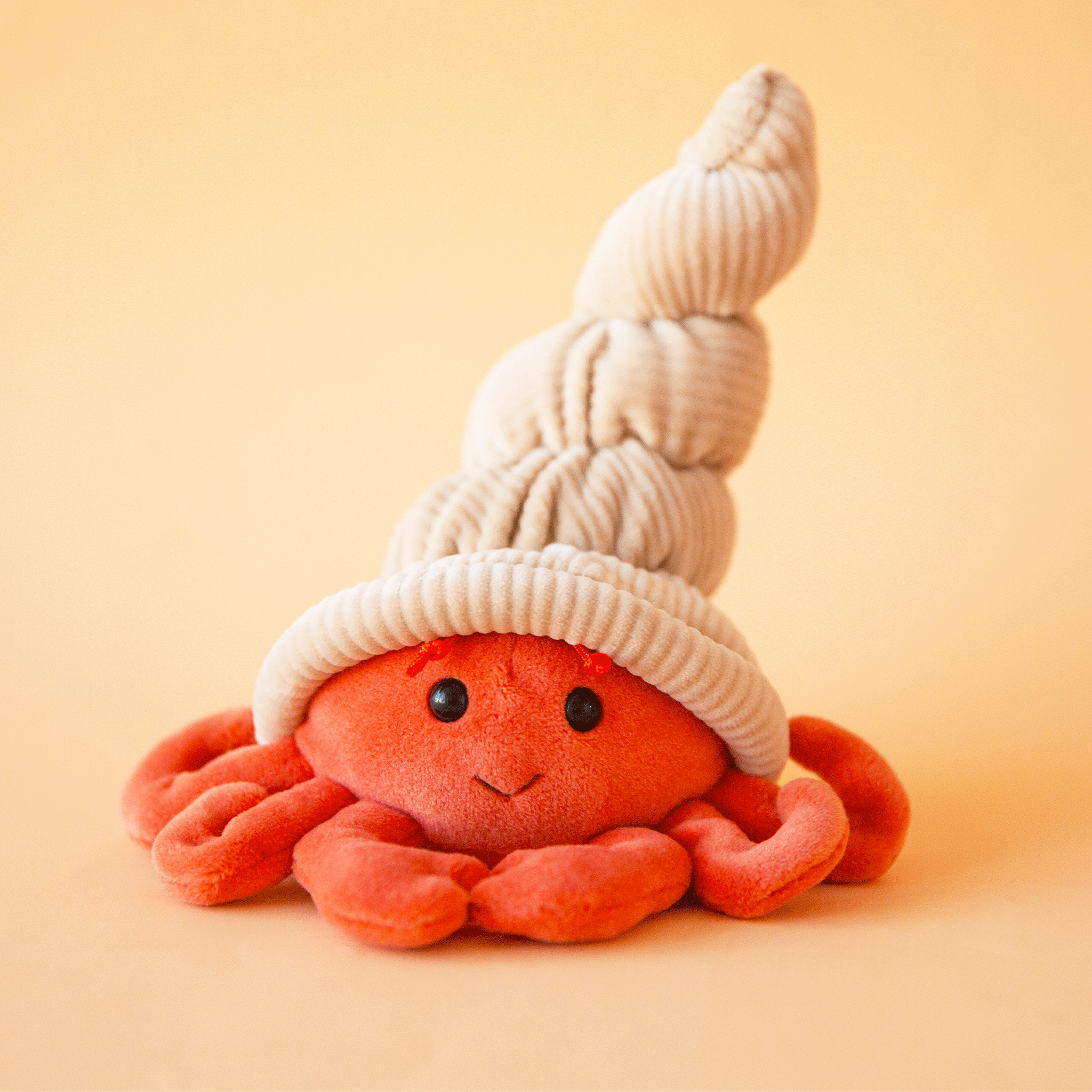 On a tan background is a red hermit crab stuffed animal toy.
