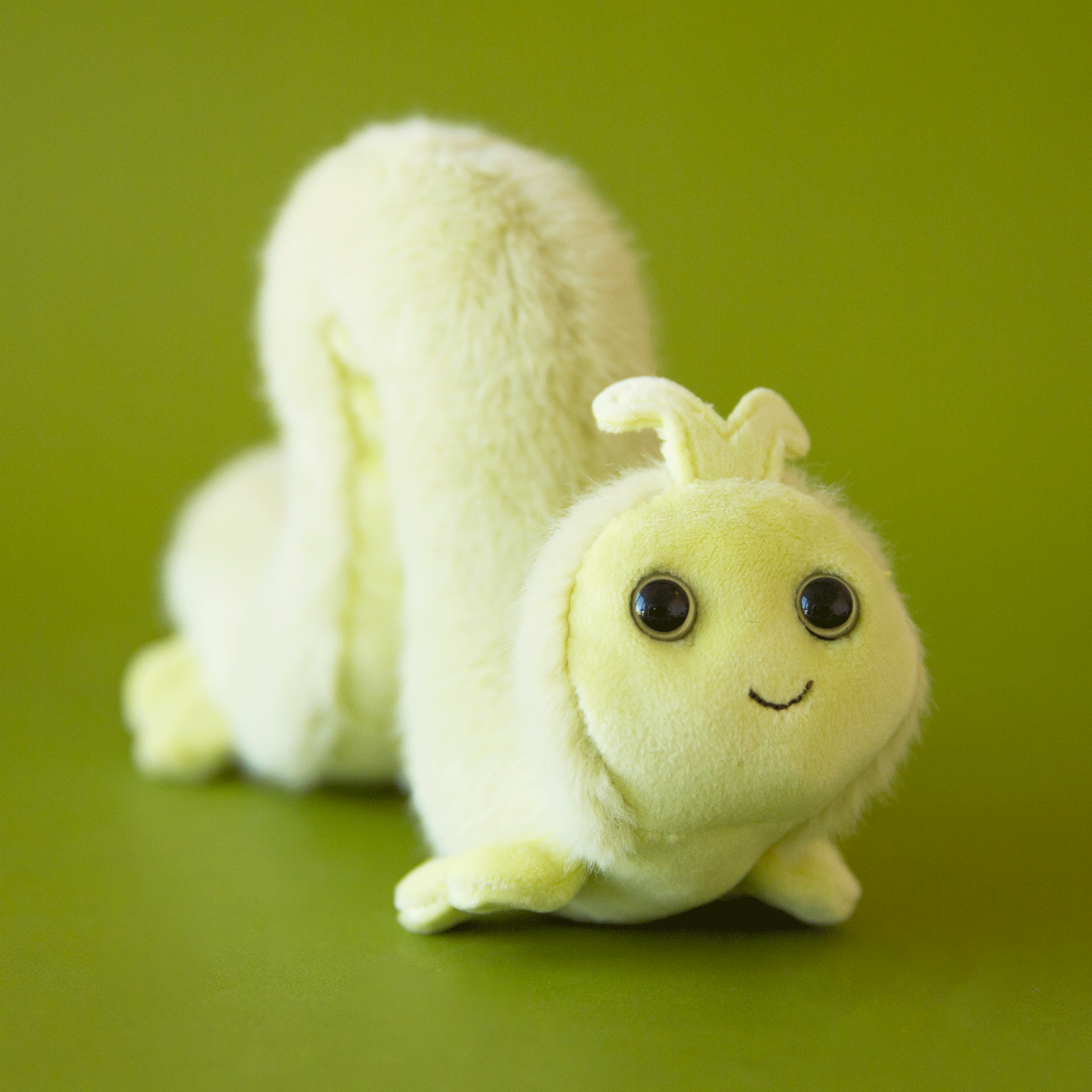 On a green background is a pastel green inchworm stuffed toy.