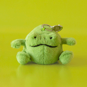 On a green background is a small green stuffed toy frog shaped bag charm.