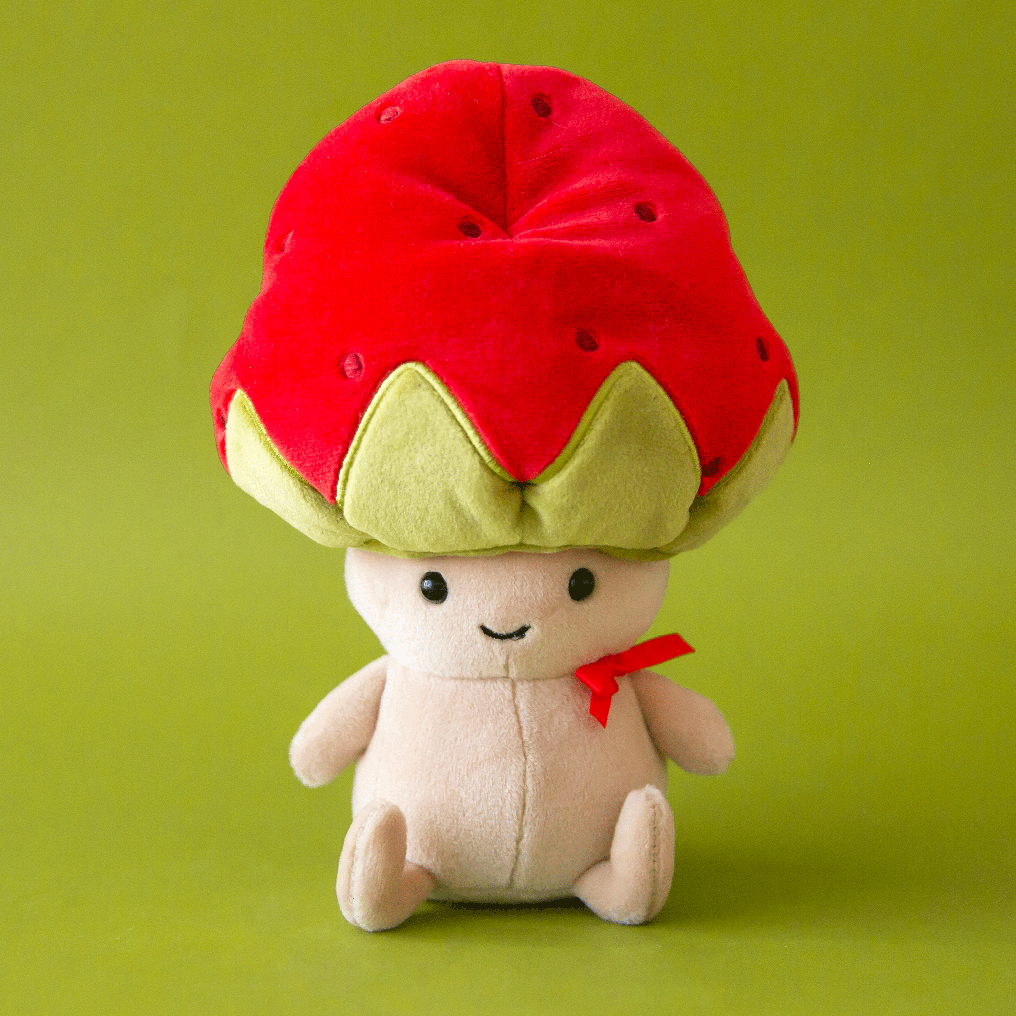 On a green background is a tan stuffed toy with a red and green strawberry shaped hat on. 