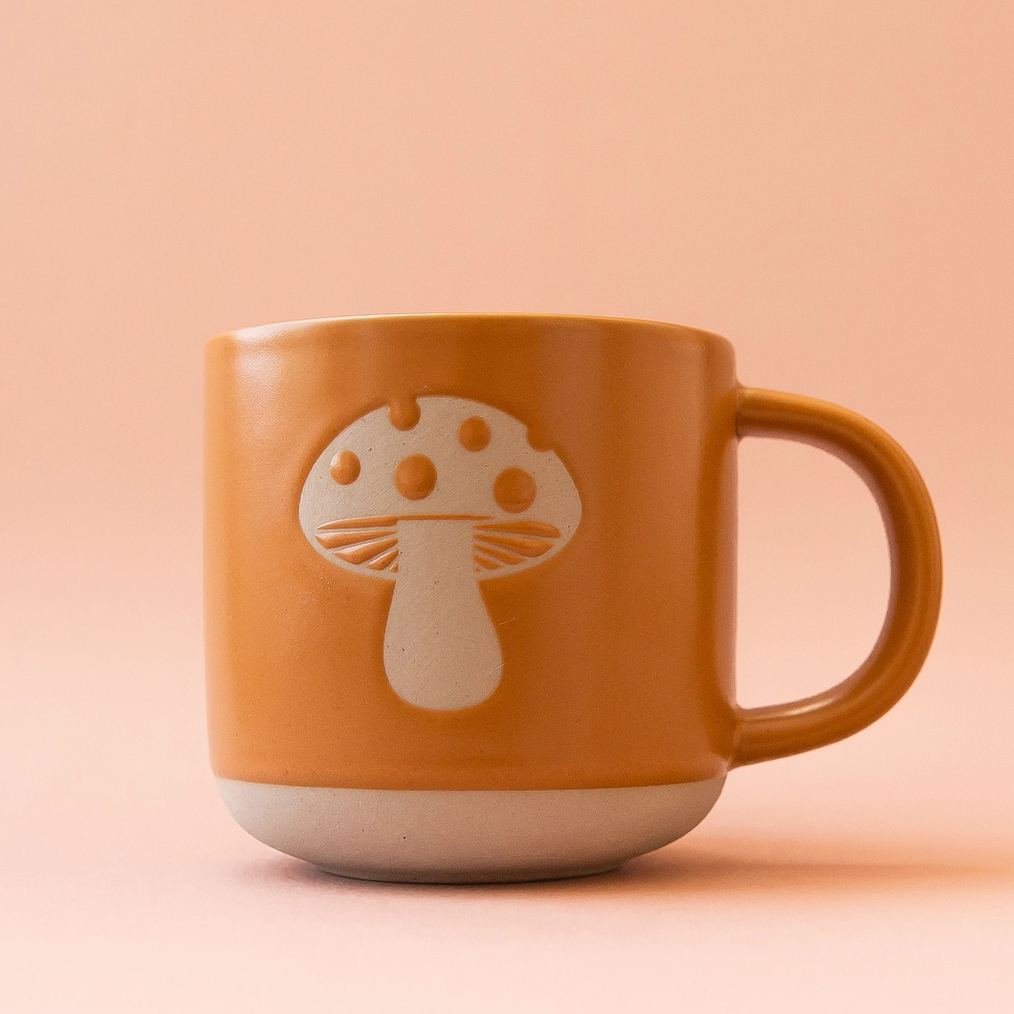 A ceramic mug with a warm brown tone with a mushroom design in the center.