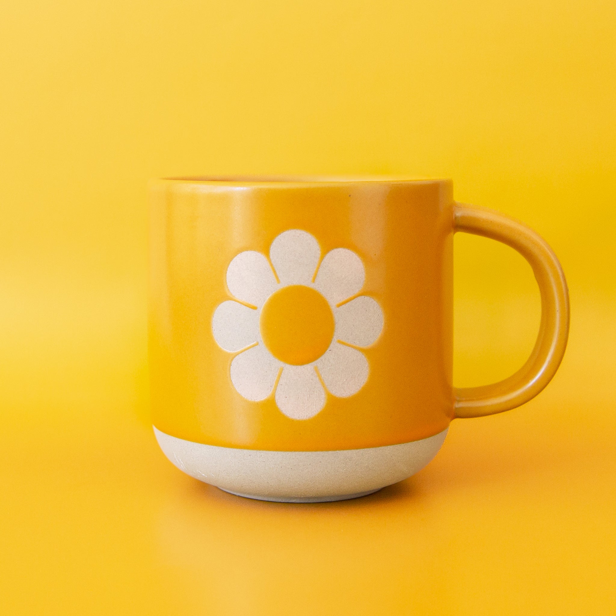 Natural clay mug painted tangerine orange with silhouette of classic daisy flower on the front. The base of the mug is unpainted, revealing natural clay.